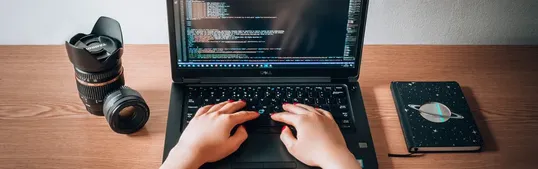 This image contains a closed notebook, a bottle of water, and a laptop in a table.